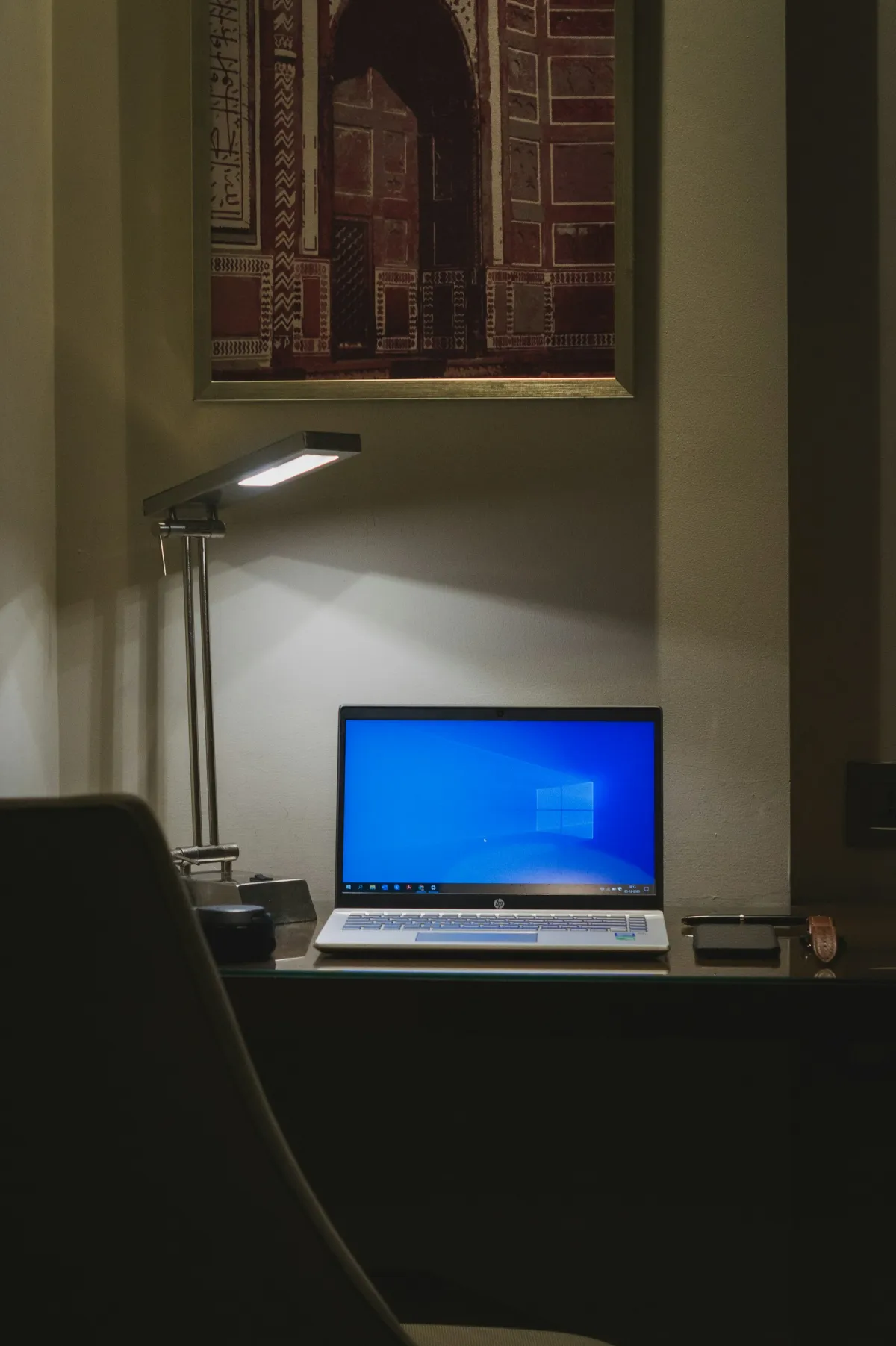 An open HP laptop on a desk beneath a reading lamp, with headphones and a phone beside it.