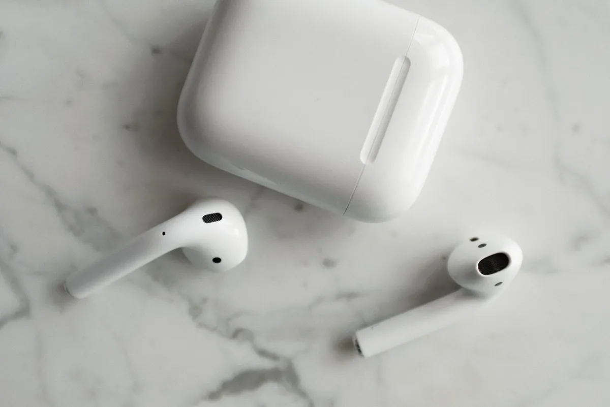 Wireless AirPods earbuds beside their charging case on marble