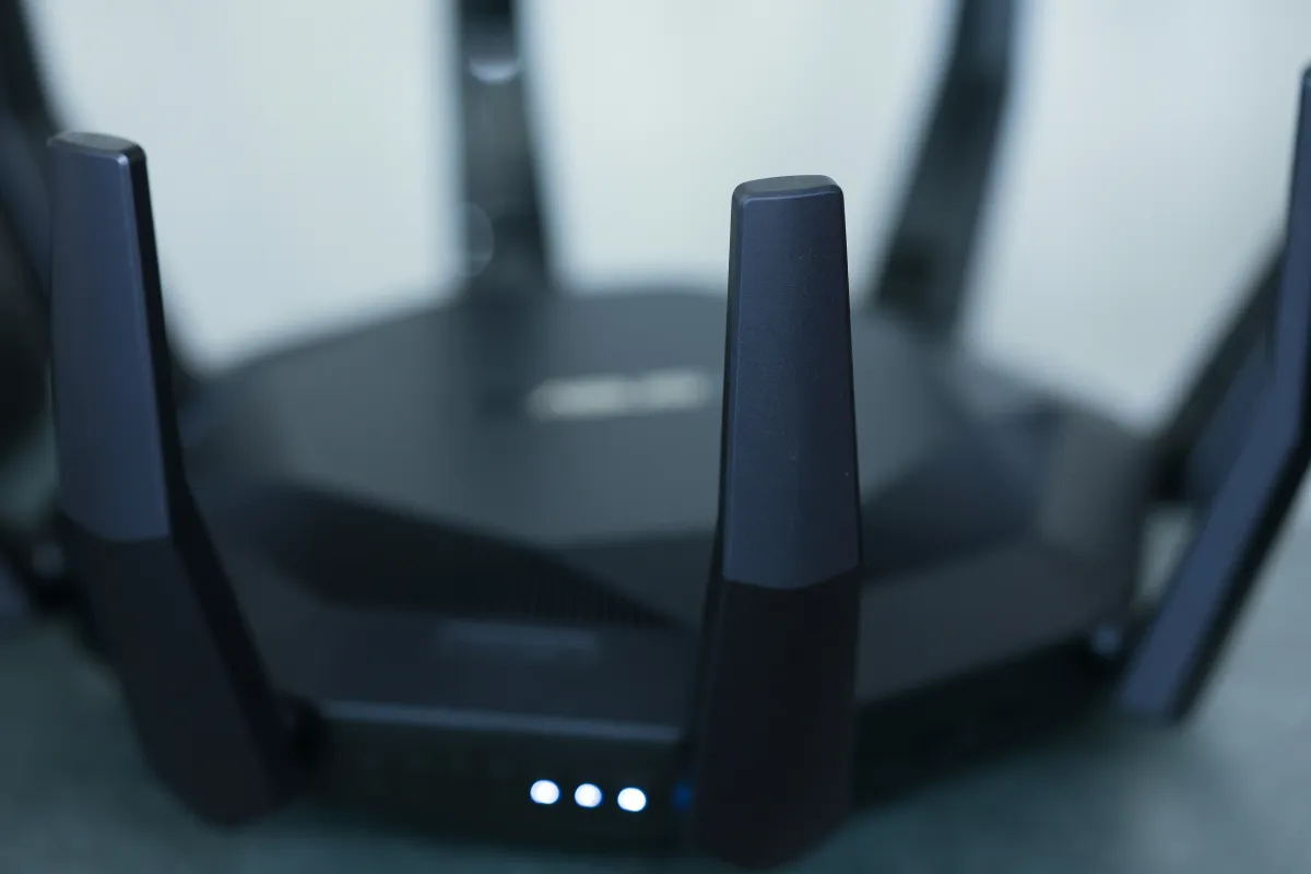 Close-up photograph of a black wireless router with upright antennas and illuminated front indicators.