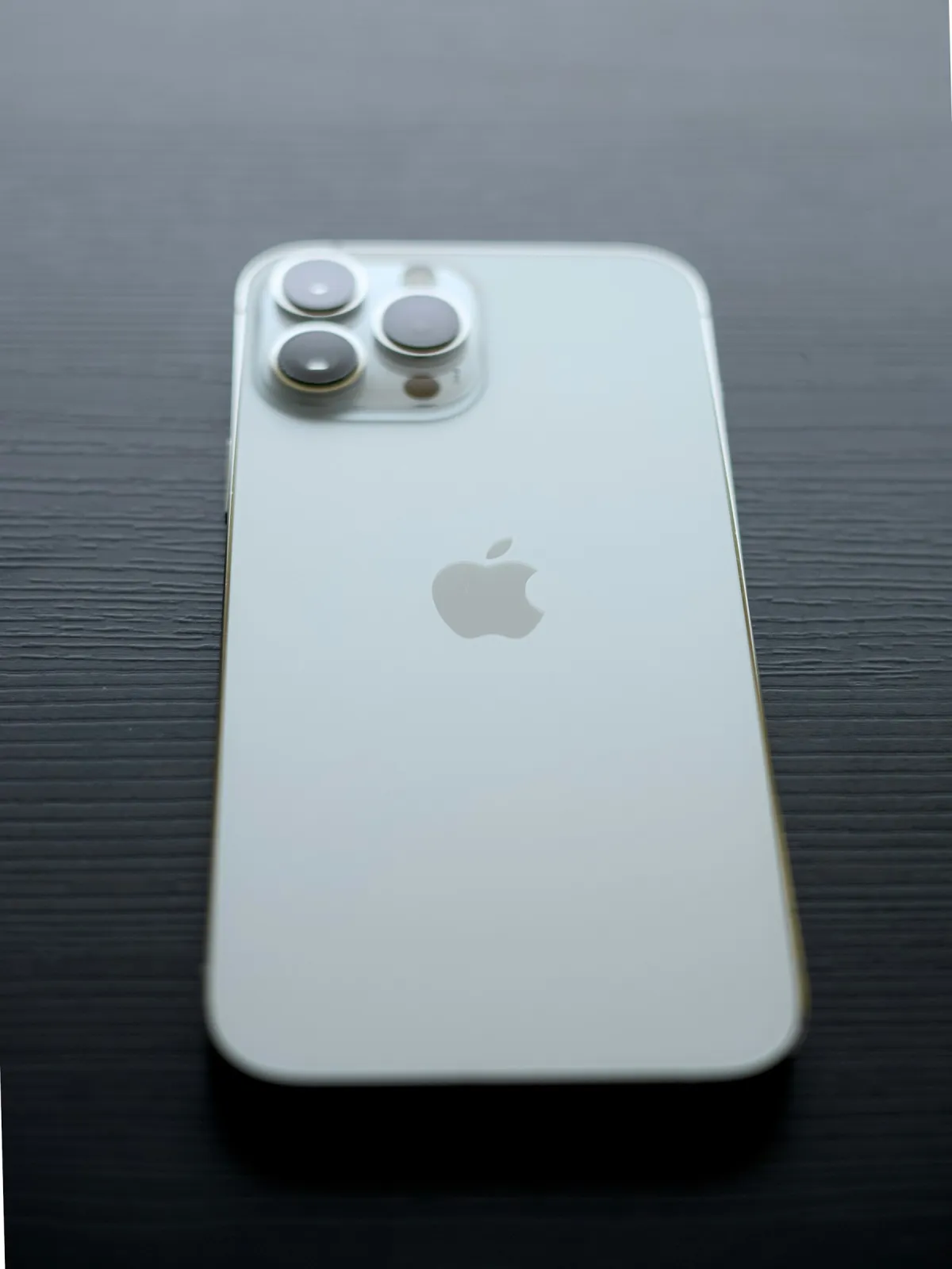 Silver iPhone lying face down on a dark wooden surface, with its rear cameras and Apple logo visible.