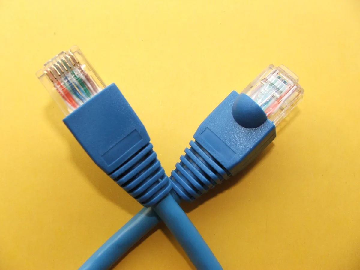 Two transparent Ethernet plugs with blue protective boots on a yellow background.