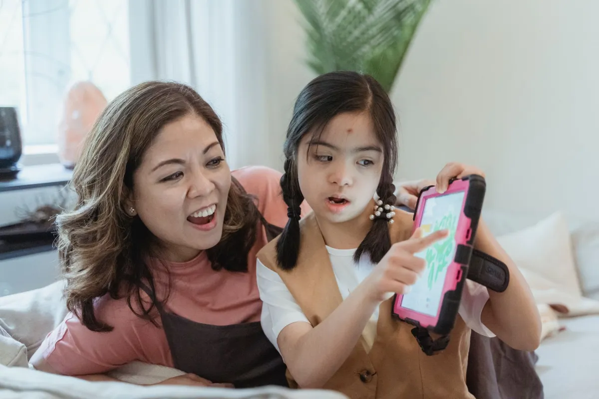 A mother and daughter use a tablet in a pink protective case while sitting together on a sofa.