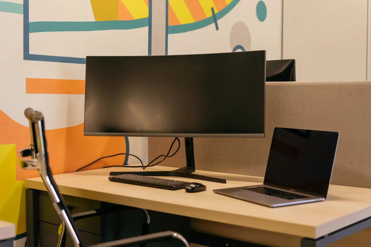 A real desktop monitor beside a laptop on a wooden desk