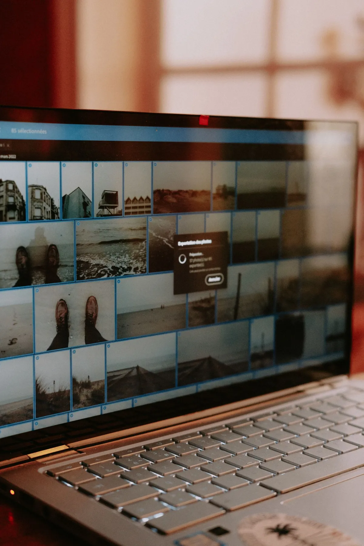 Laptop showing a grid of photographs and an export dialog in photo-editing software