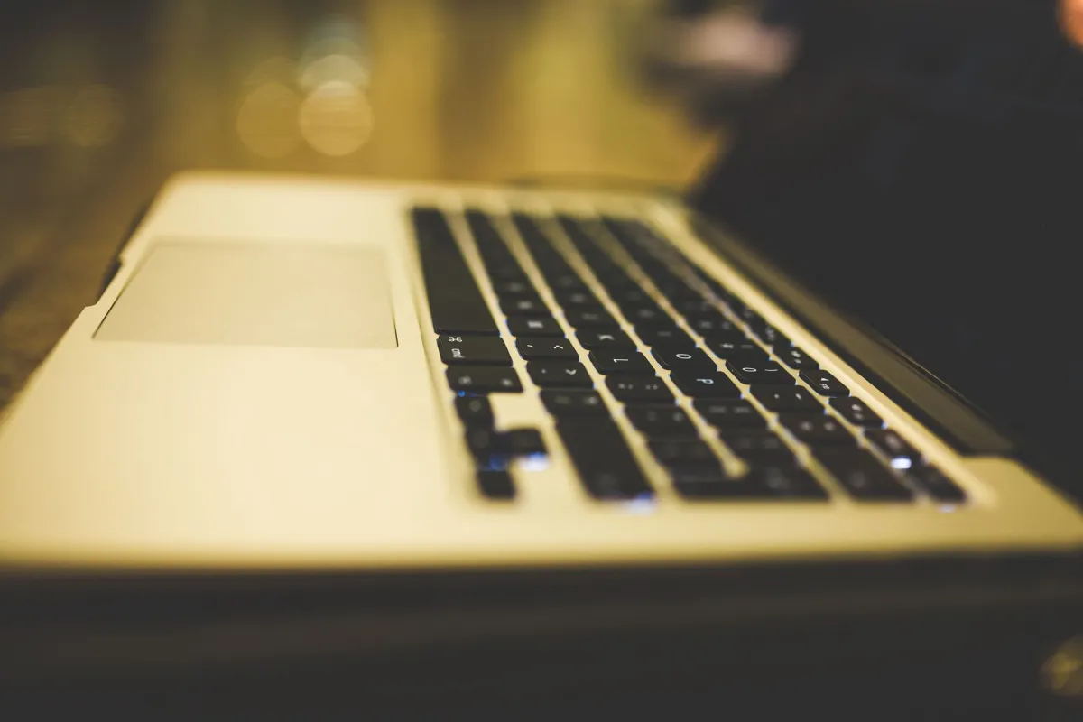 Side view of an open silver MacBook with black keys, a trackpad and a dark reflective display.