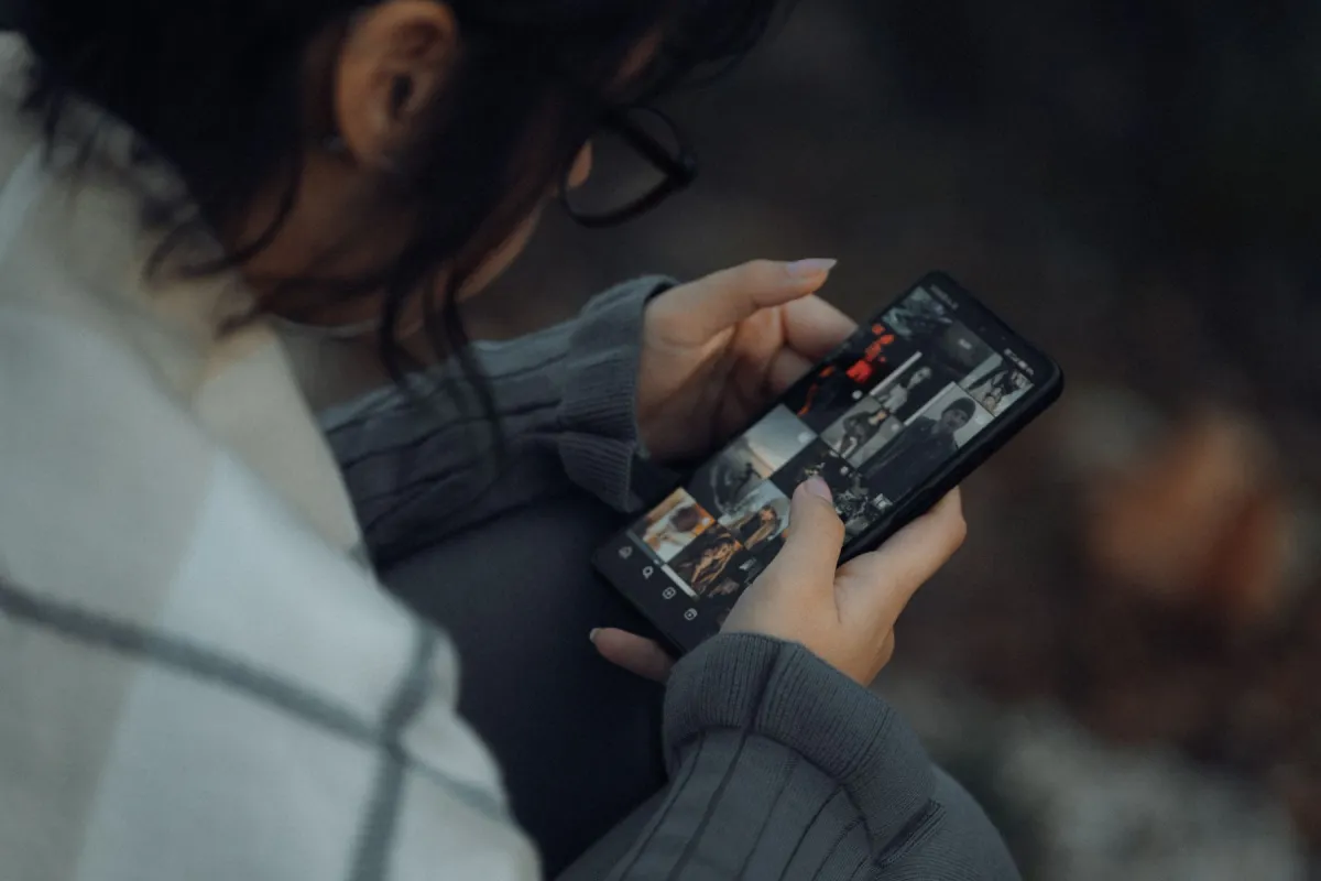 A person browsing a grid of photographs on a smartphone outdoors.