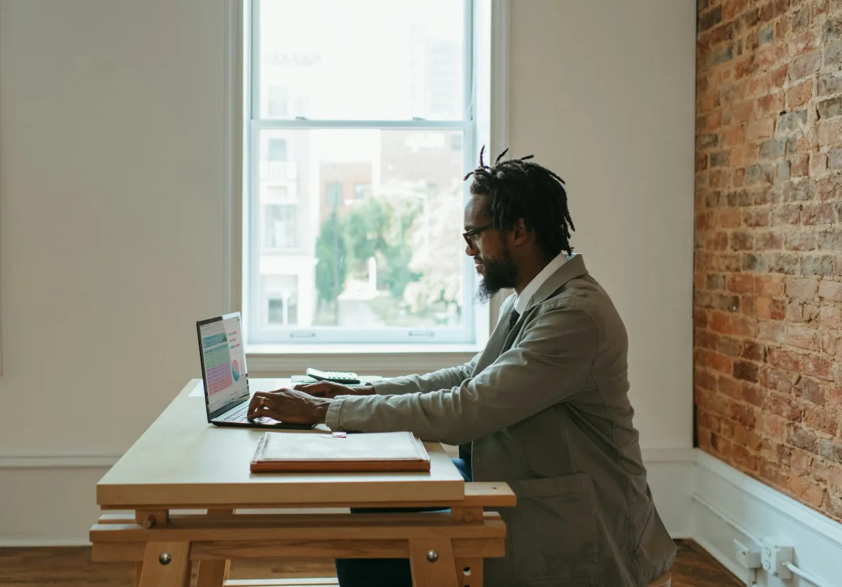Person working on a laptop at a wooden desk with a closed folder and calculator beside it.