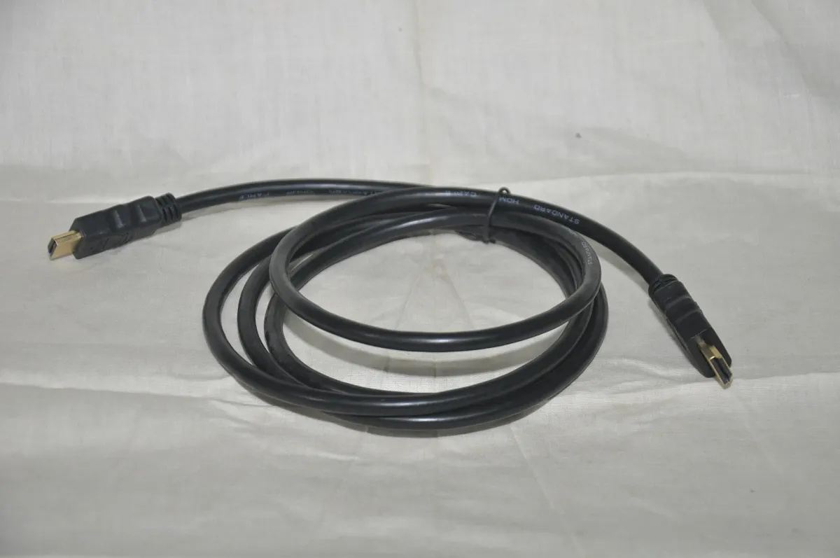 A coiled black HDMI cable with both gold-colored connector ends visible on pale fabric.