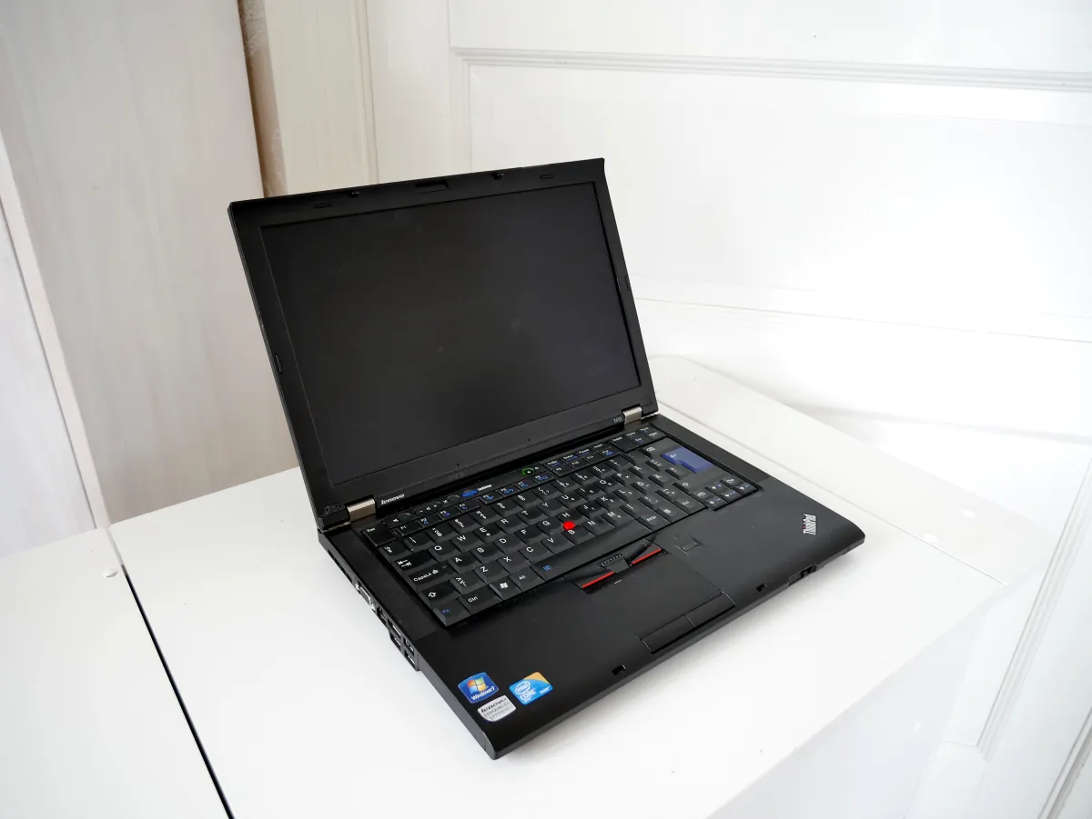 Older black ThinkPad laptop open on a white table with its display dark.