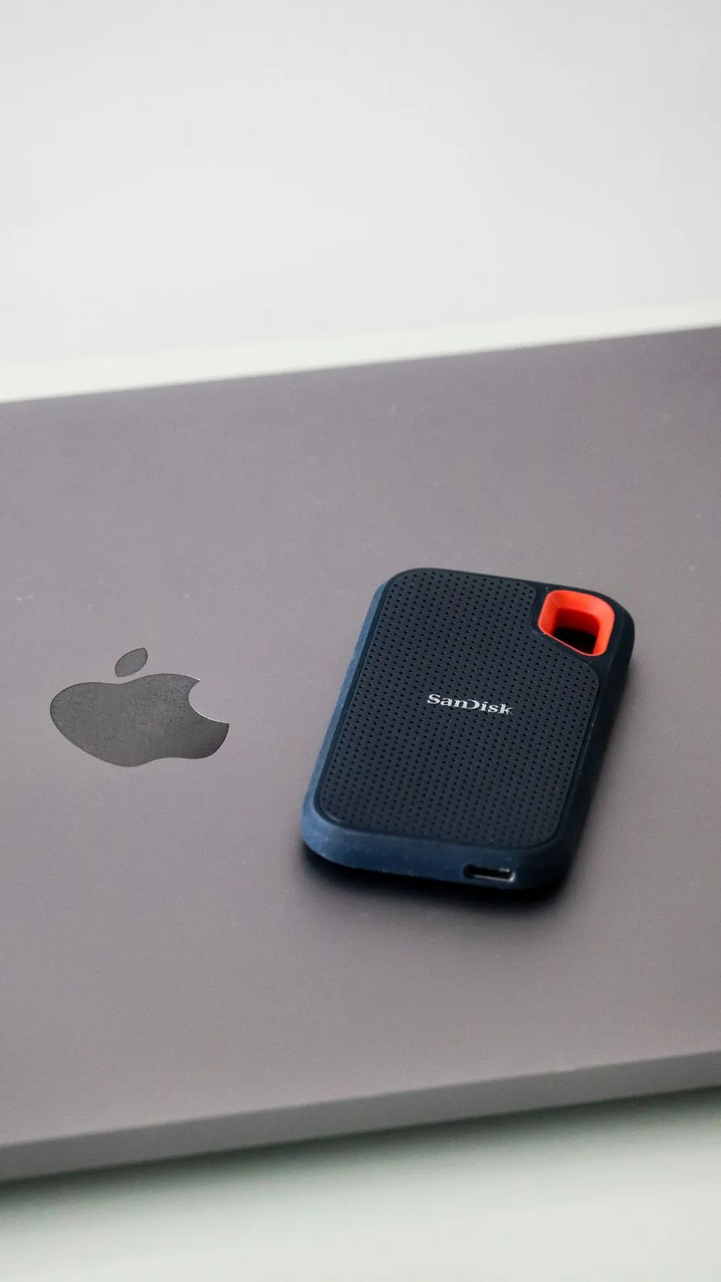 A rugged SanDisk portable SSD resting on a laptop