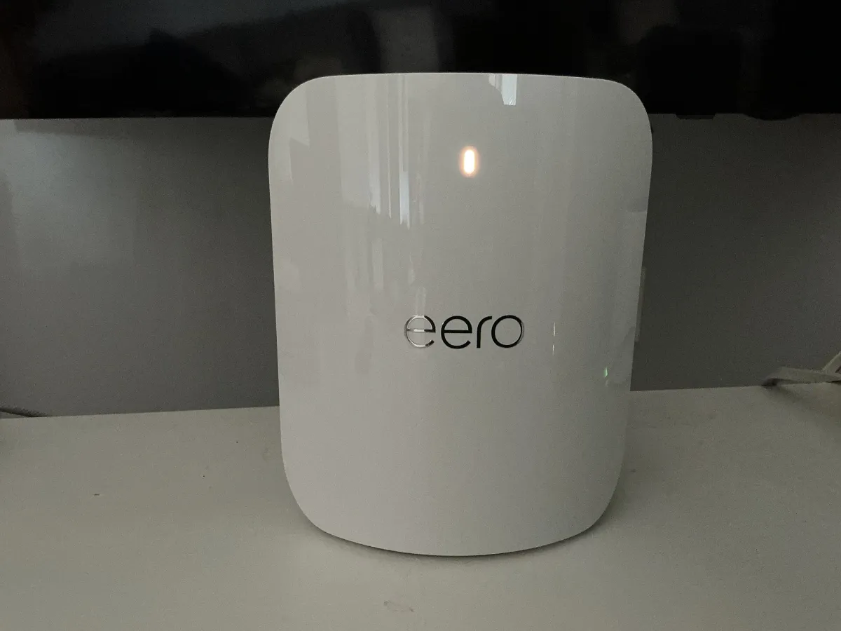 White eero router with an illuminated status light standing on a shelf.