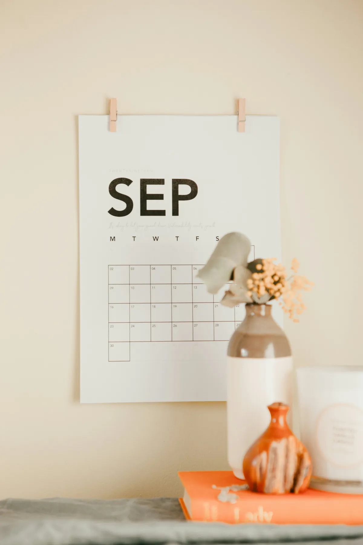 A paper September 2019 calendar clipped to a wall above a desk with vases and an orange book.