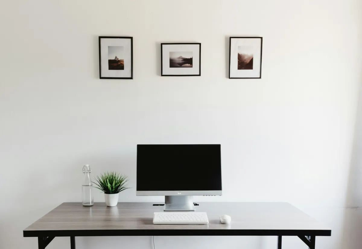Desktop monitor with a dark screen, keyboard and mouse on an uncluttered wooden desk.