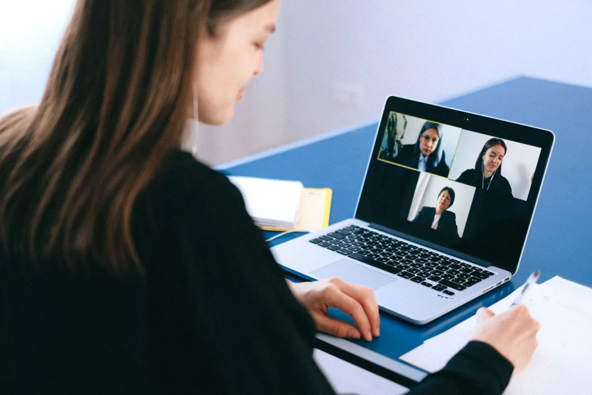 Person taking notes beside a laptop showing a group video call