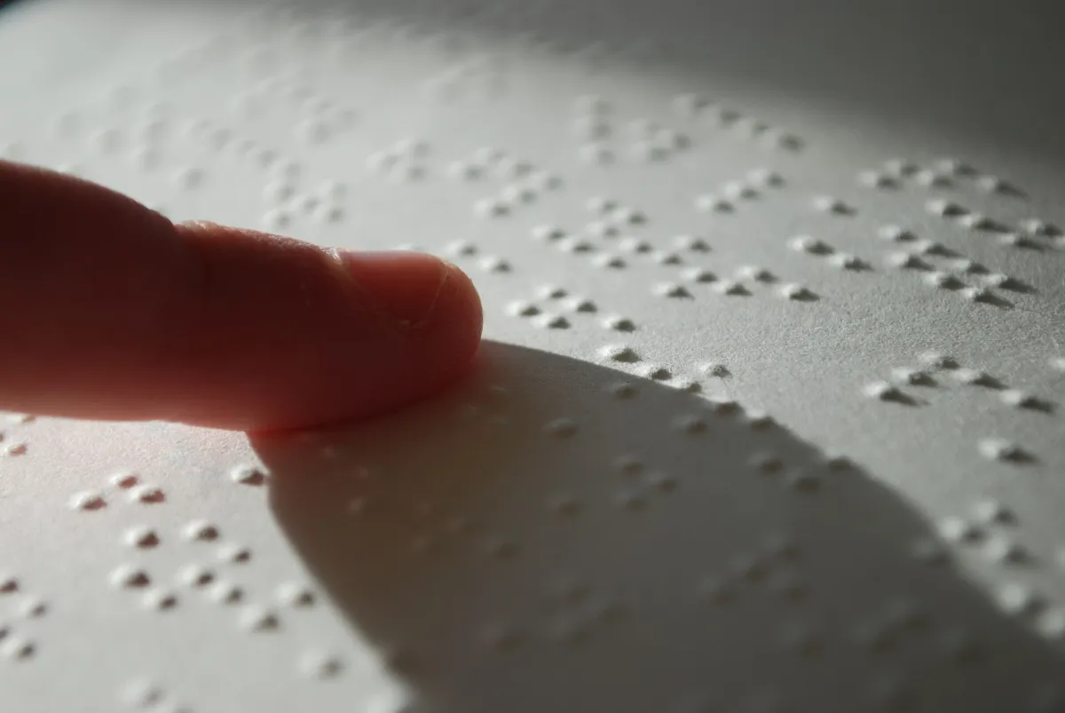 Close-up of a fingertip touching raised braille dots on a sheet of paper.
