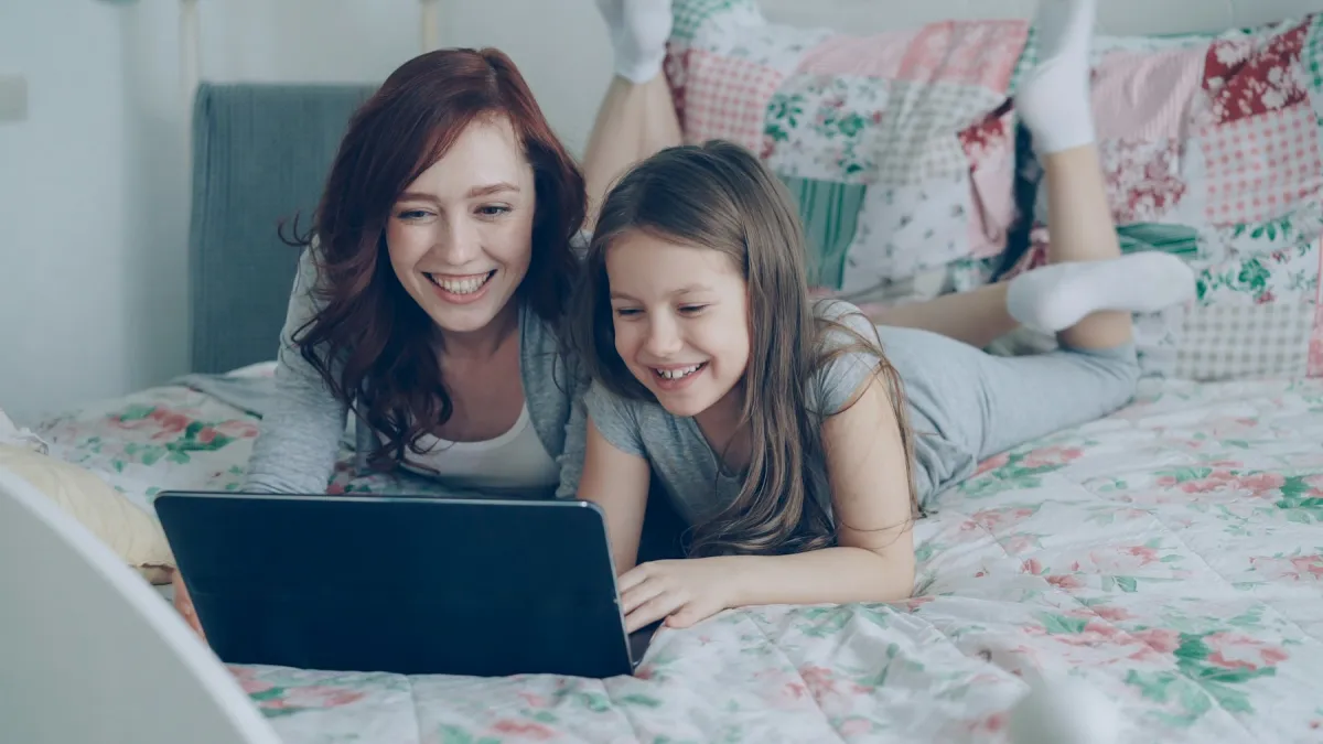 A mother and daughter smiling together while looking at a laptop at home.