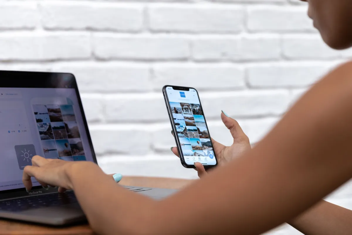 Person holding a smartphone while using a laptop at a table