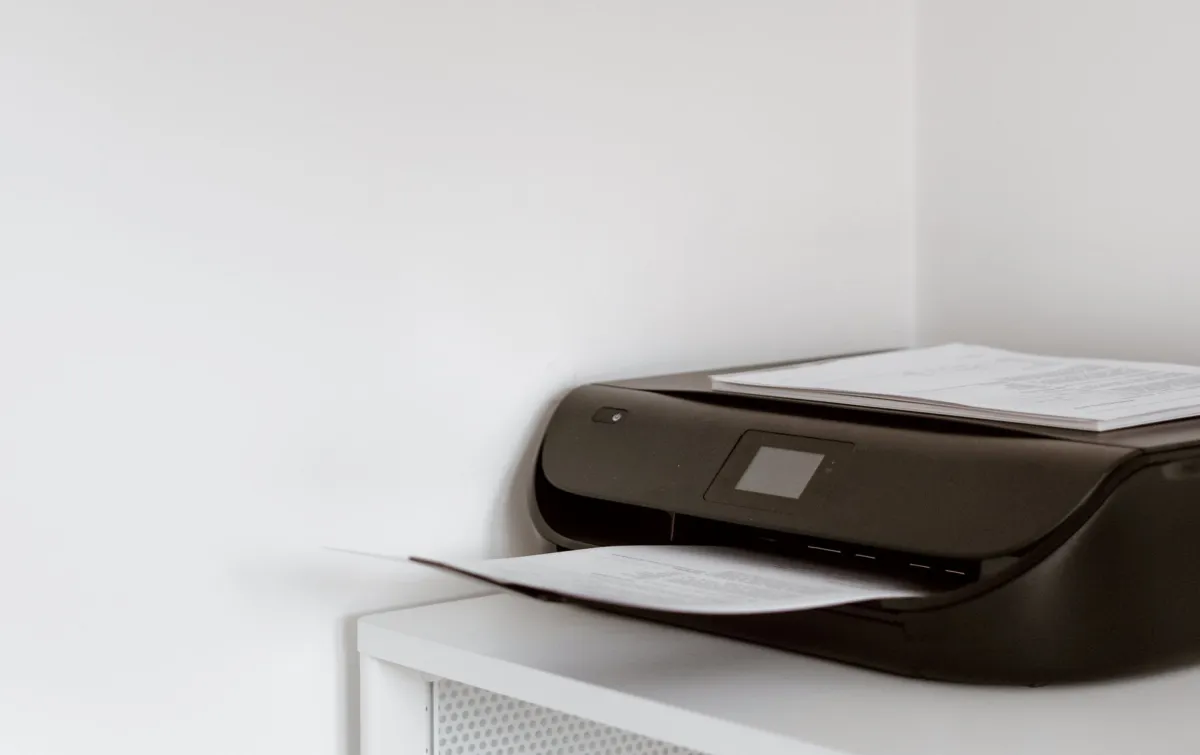 Black office printer with a sheet of paper on a white cabinet
