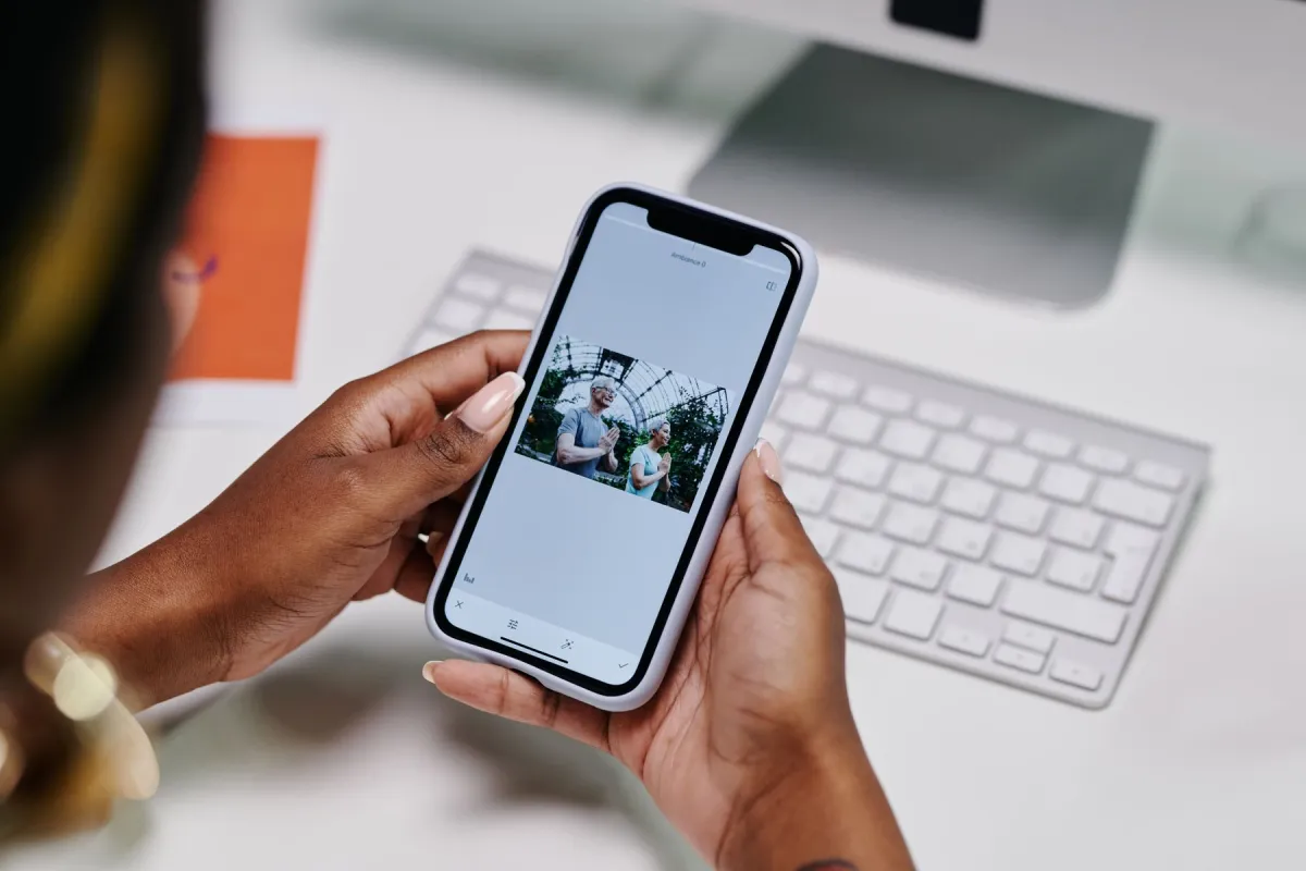 Hands holding a smartphone with a photograph open beside a keyboard
