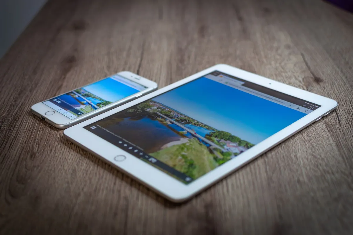 A white tablet and smartphone displaying landscape photographs on a wooden table.