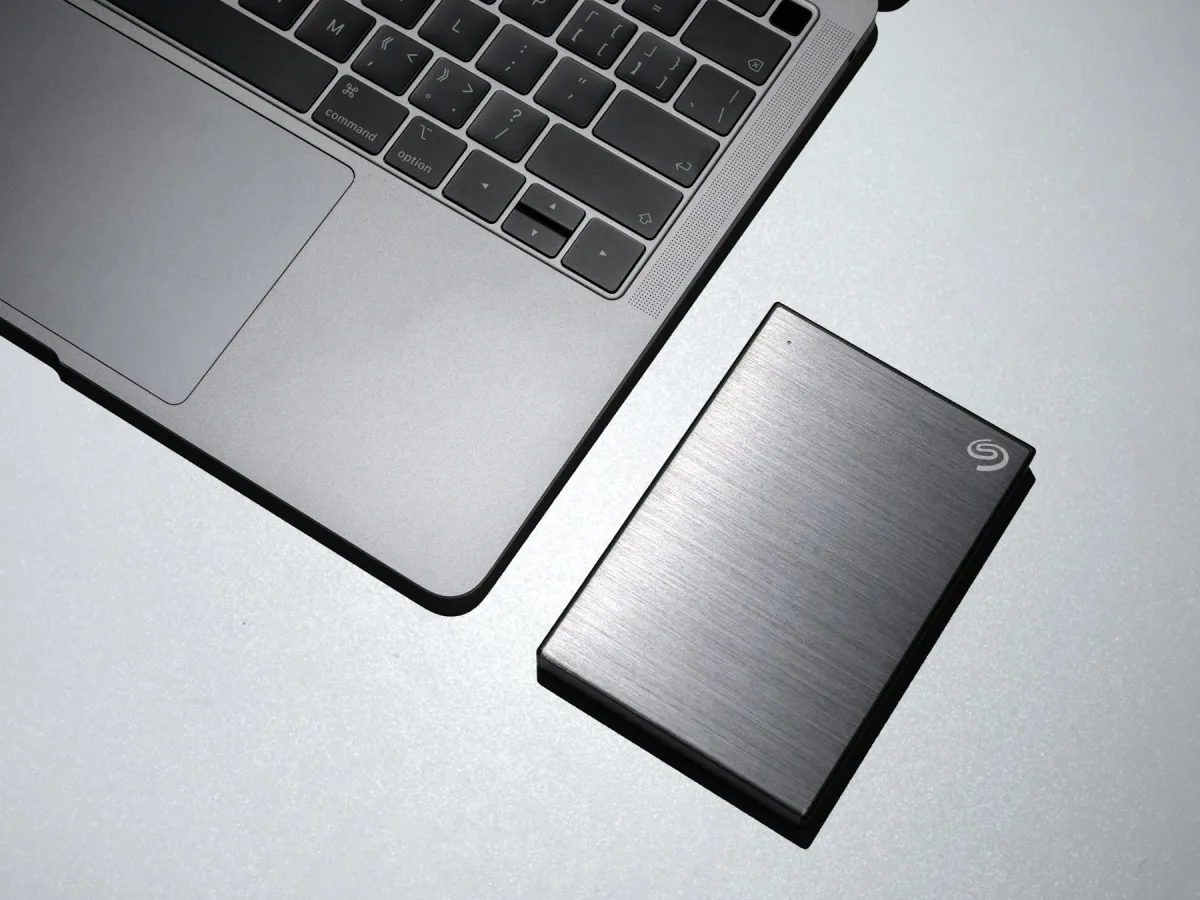 A silver MacBook beside a brushed-metal external hard drive on a pale desk.