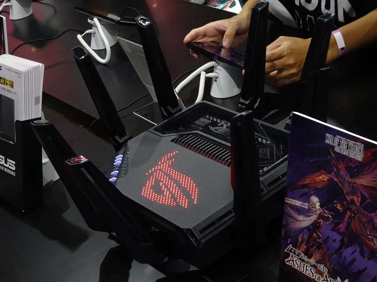 ASUS ROG router with multiple antennas on an exhibition counter while a visitor uses a phone