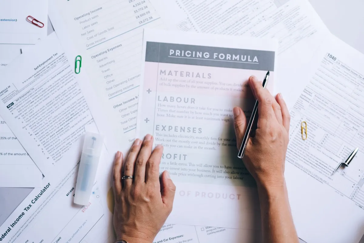 Hands holding a pen over pricing worksheets and financial paperwork on a desk.