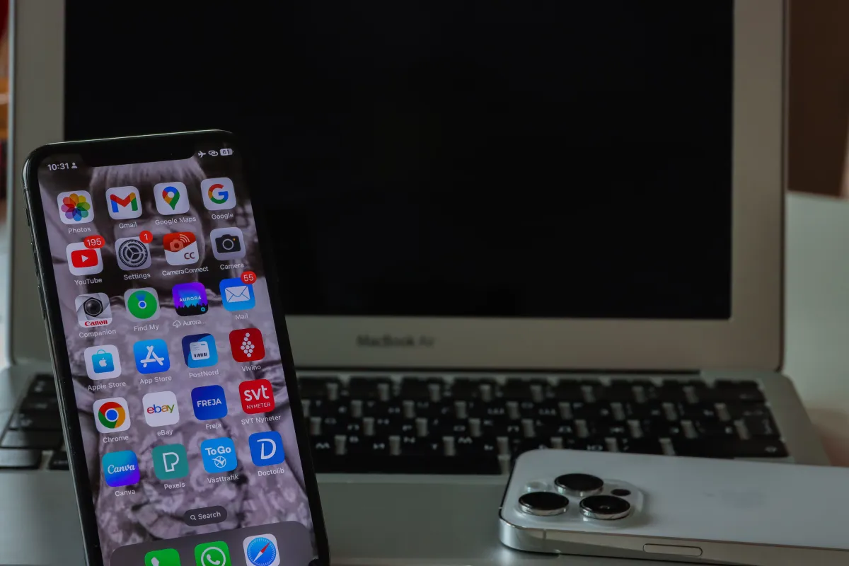 A phone showing Google app icons beside an open laptop with a dark screen and a second phone lying face down.