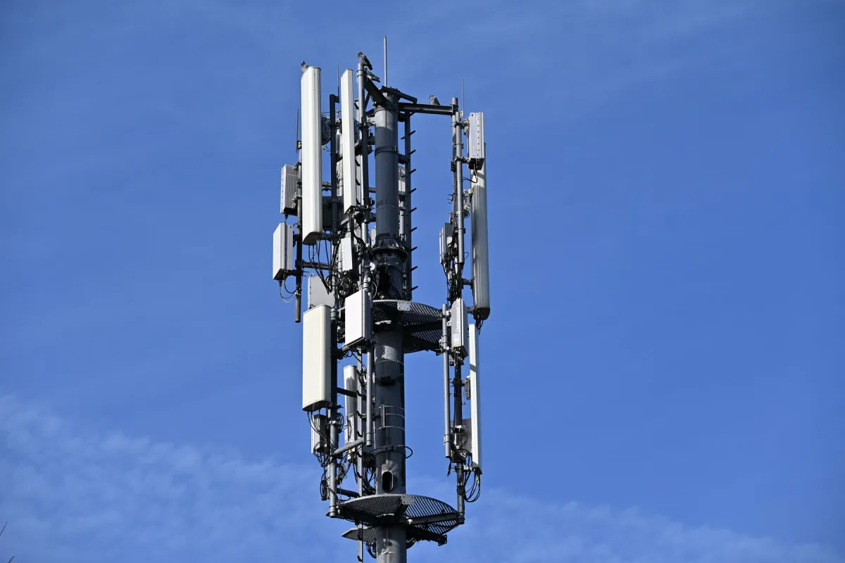 Cellular tower with vertical panel antennas, cables and perched birds against a clear blue sky.