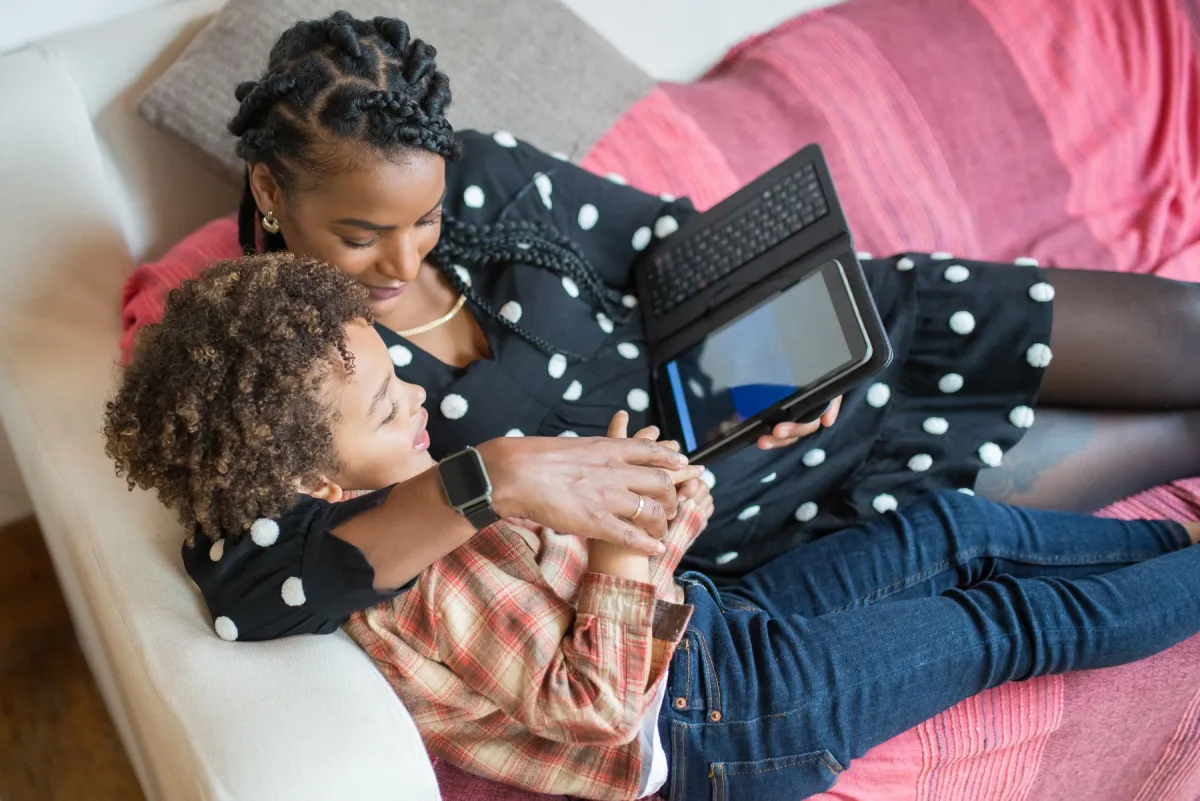 An adult and child sitting together on a sofa, looking at a tablet in a keyboard case.
