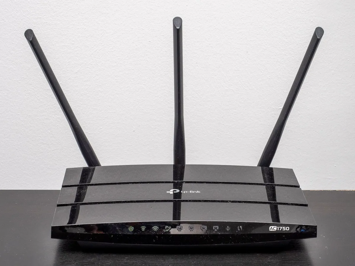 Black TP-Link AC1750 wireless router with three upright antennas on a dark surface against a pale wall.