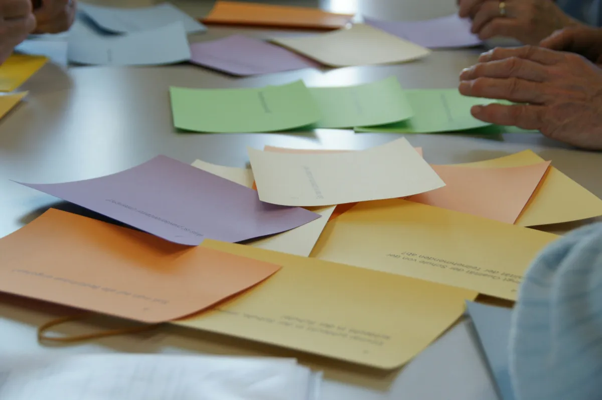 Hands sorting overlapping sheets of colored paper on a table.