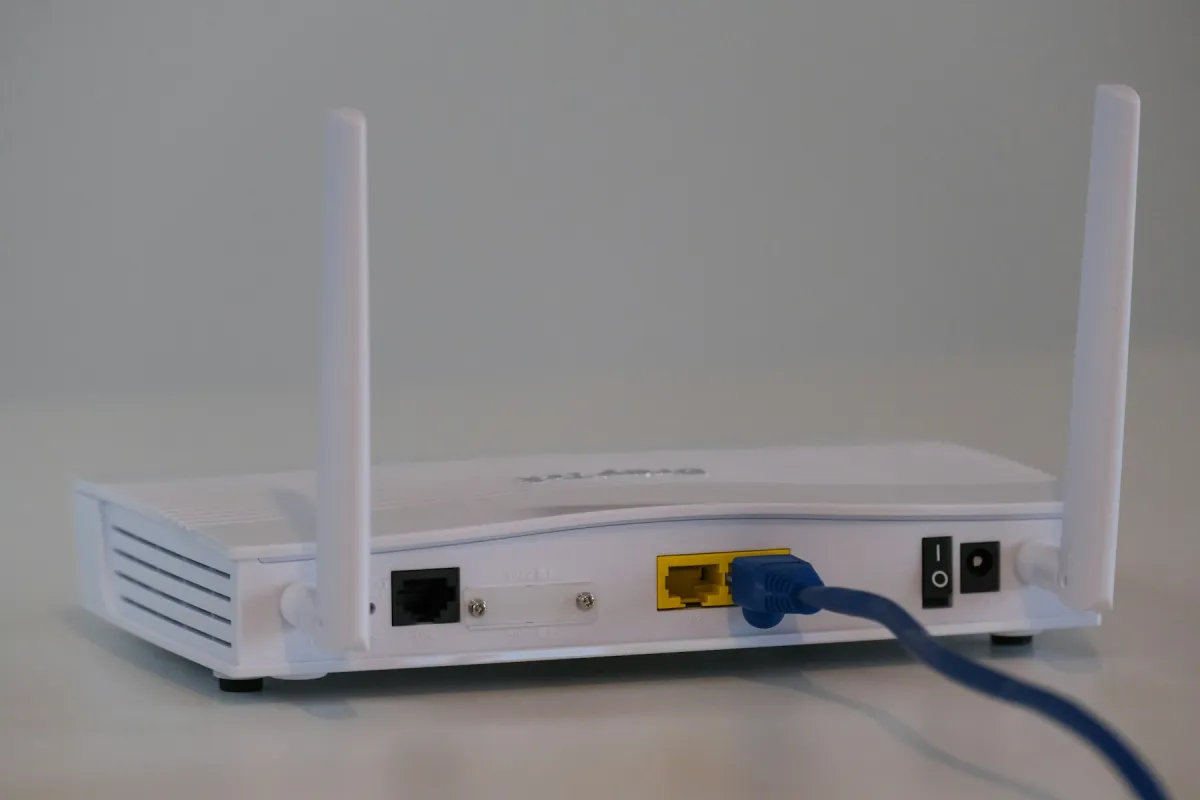 White broadband router with antennas and an attached Ethernet cable on a table