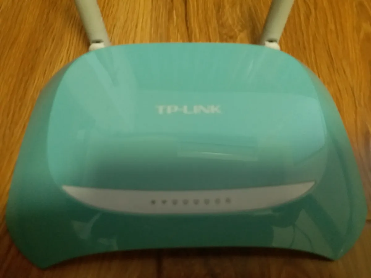 A green TP-Link router with external antennas resting on a wooden surface.