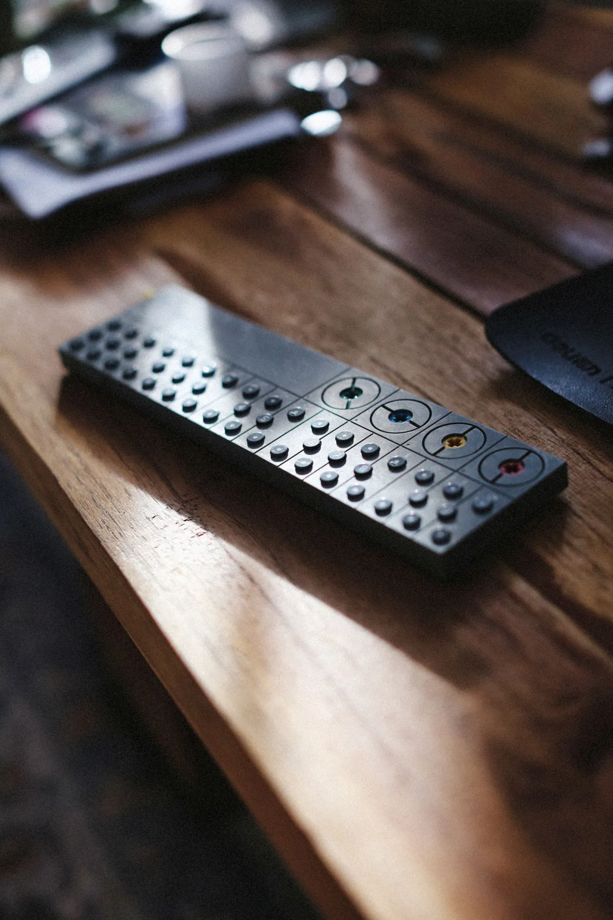 Remote-shaped control with round buttons resting on a wooden table in sunlight.
