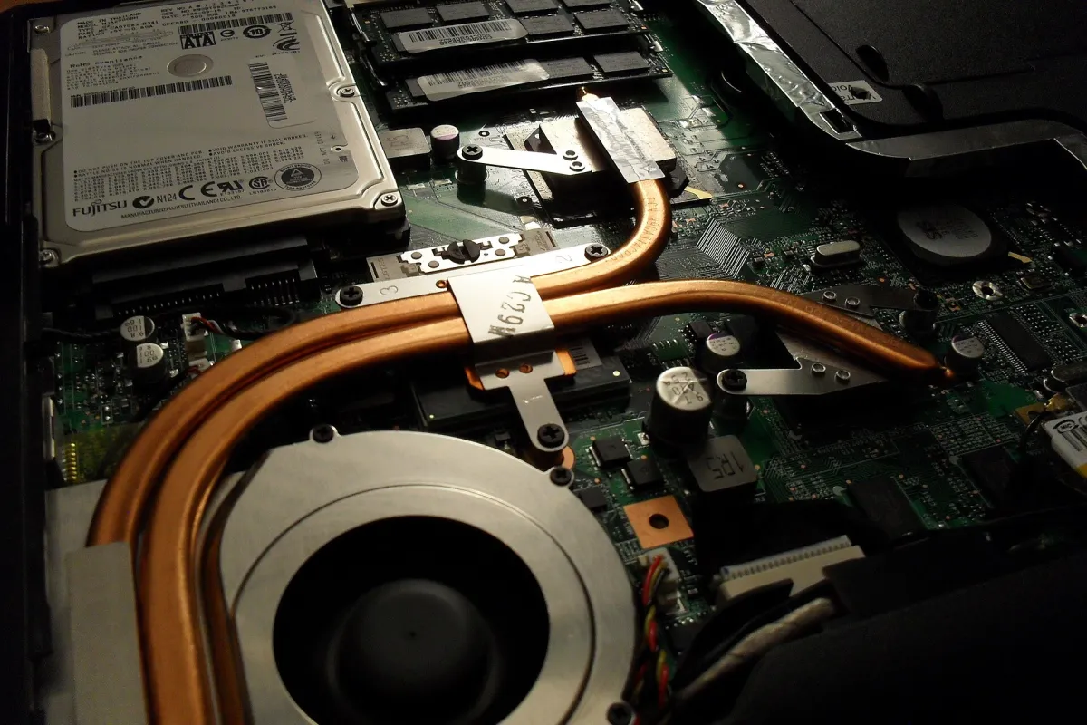 Copper heat pipes and a circular cooling-fan housing inside an opened laptop, beside memory modules and a hard drive.