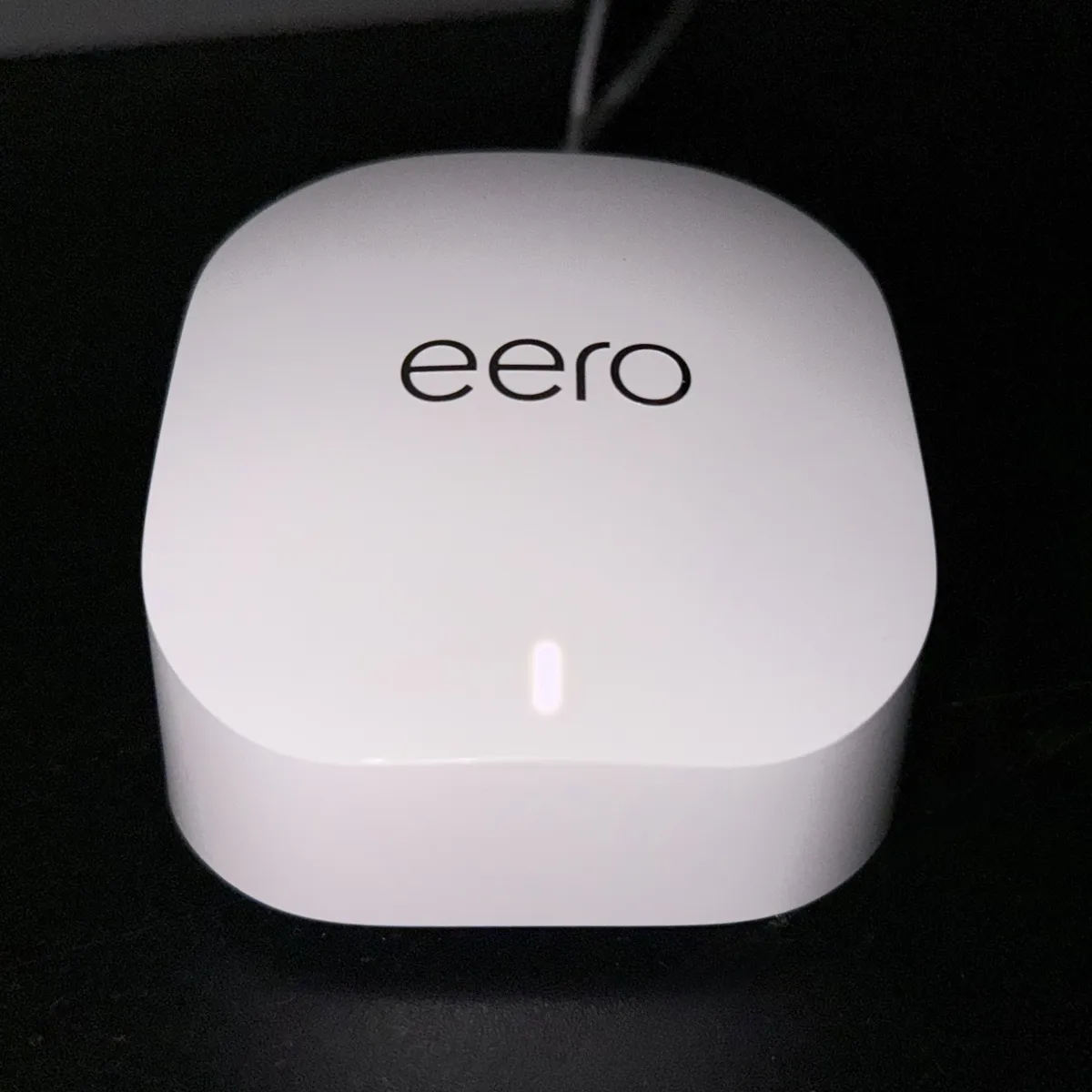 White eero mesh Wi-Fi router photographed on a dark surface, with its logo and front status light visible.