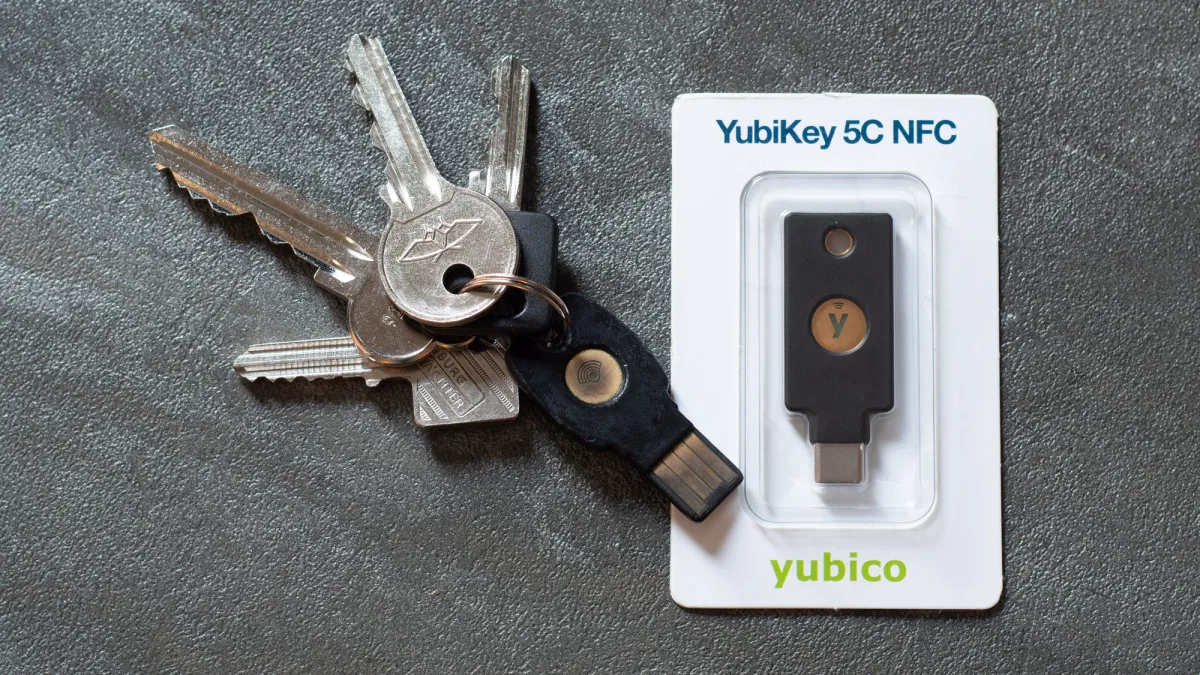 A security key on a household key ring beside a packaged YubiKey 5C NFC on a grey surface.