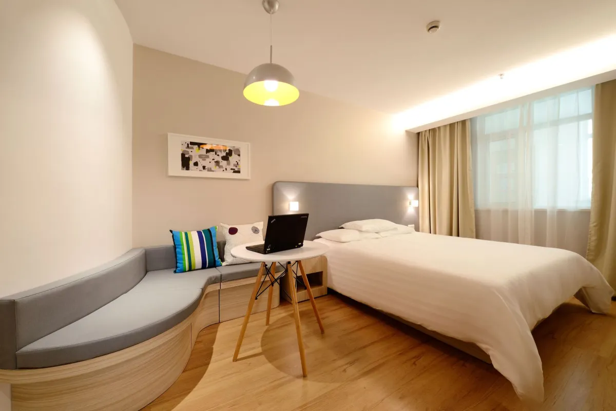 Black laptop on a small round table beside a hotel bed and curved sofa.