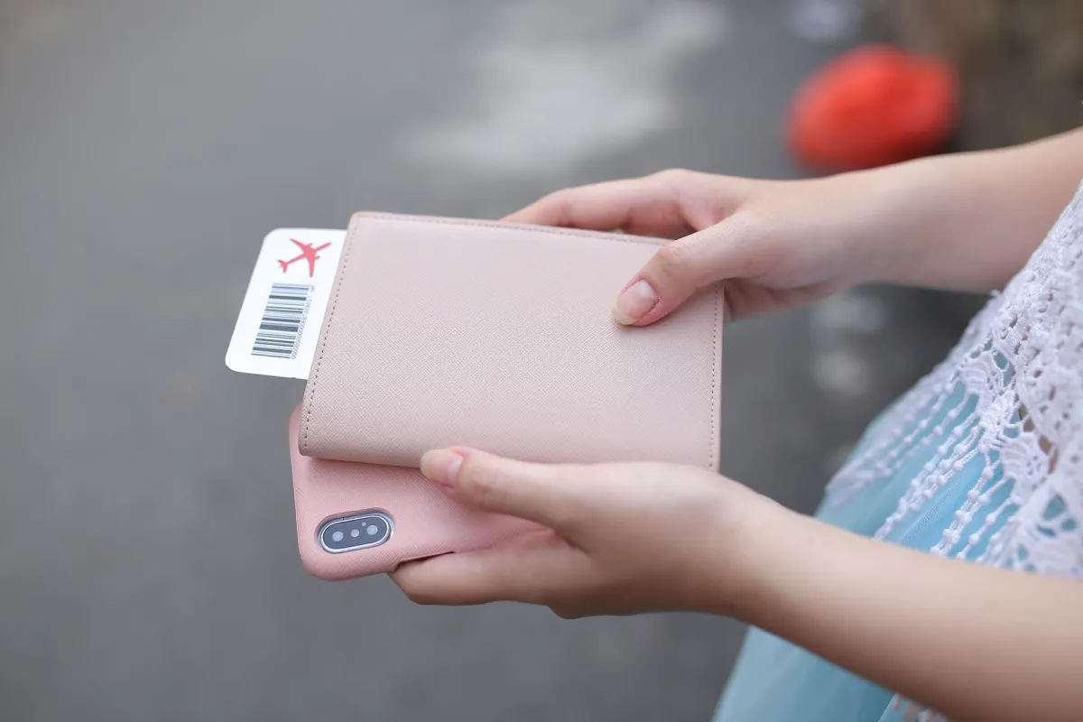 Hands holding a pink phone case and passport wallet with a boarding pass tucked inside.