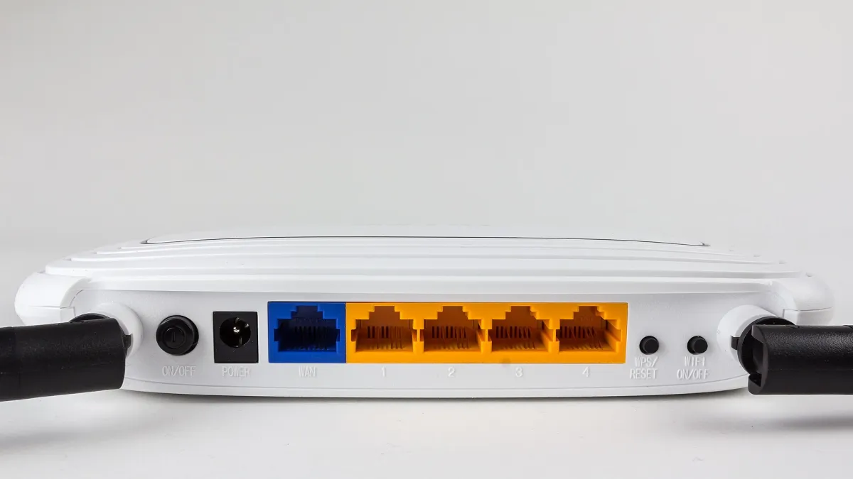 Rear of a white TP-Link router showing a blue WAN socket, four yellow numbered LAN sockets, power and wireless controls.