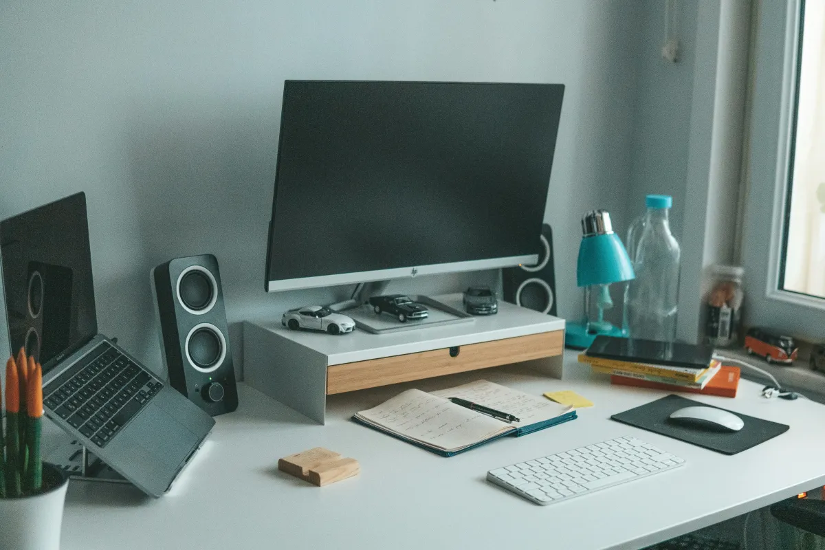 External HP monitor with a dark screen beside an open laptop, speakers, notebook and white keyboard on a desk