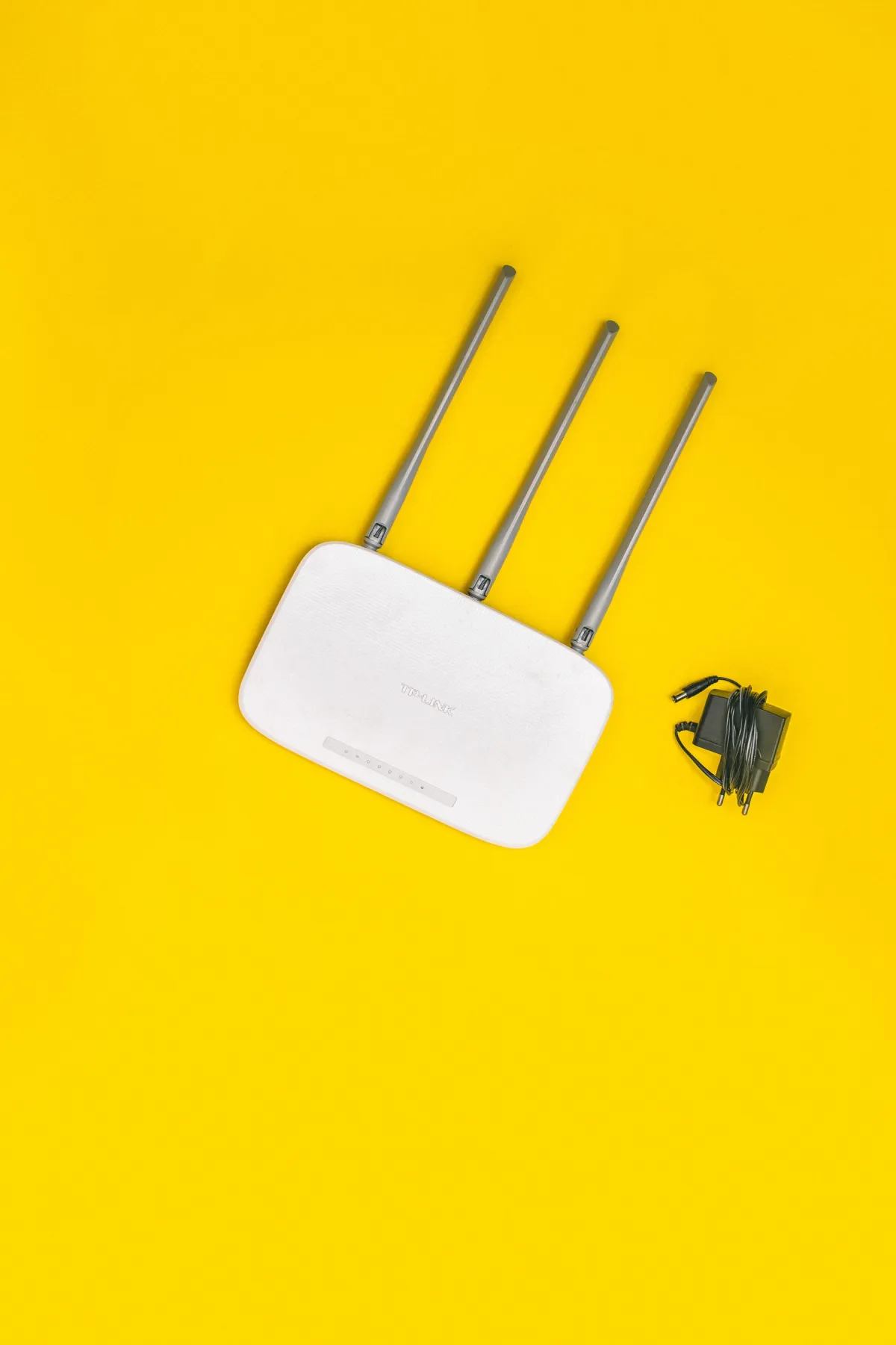 White router with three antennas and cables on a yellow surface