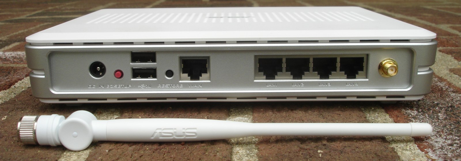 Rear of an ASUS WL-500g Premium with a separate WAN socket and four sockets labelled LAN 1 to LAN 4; its detached antenna rests in front.