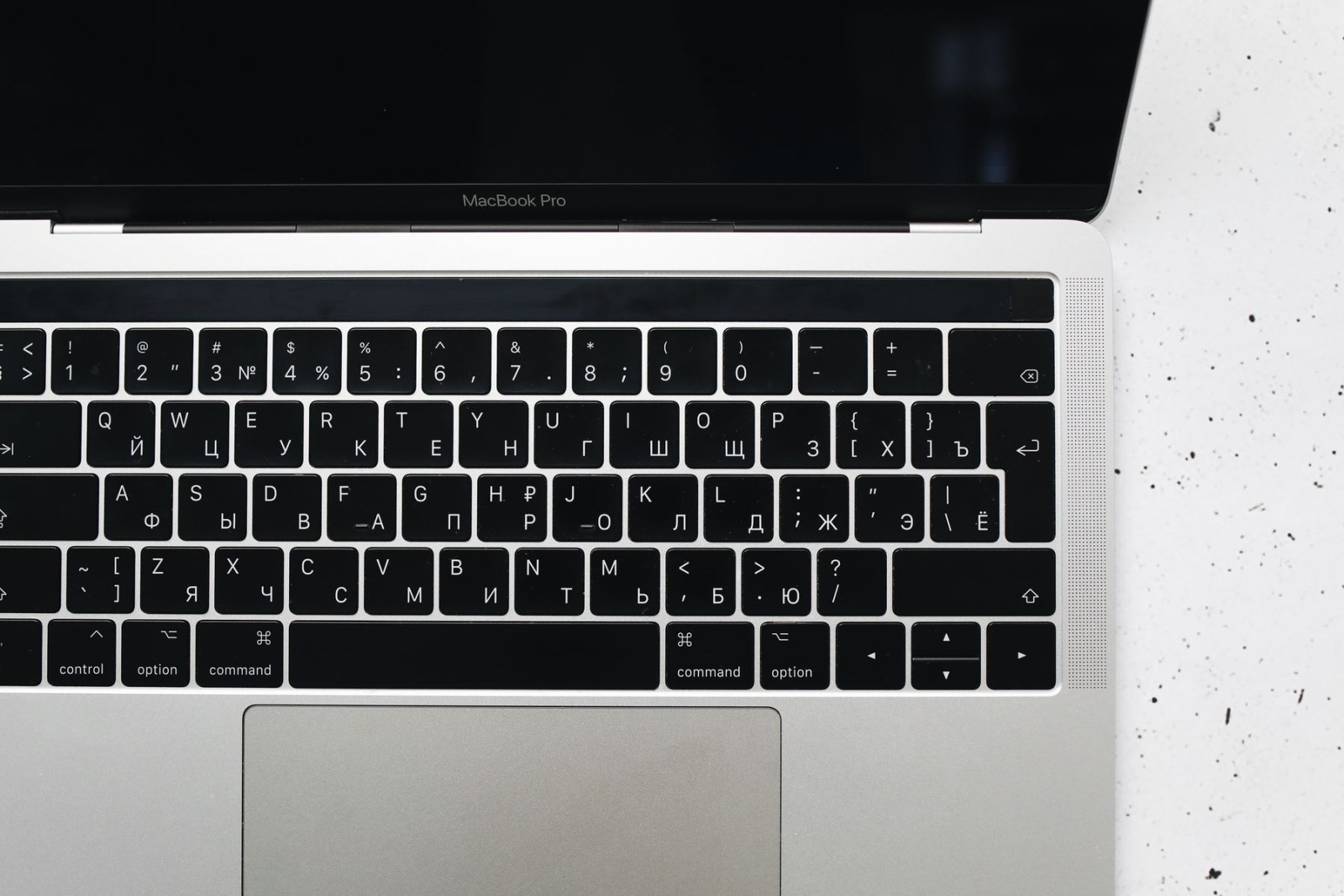 Overhead view of a MacBook Pro keyboard with Latin and Cyrillic key legends, narrow gaps and a perforated speaker grille on the right.