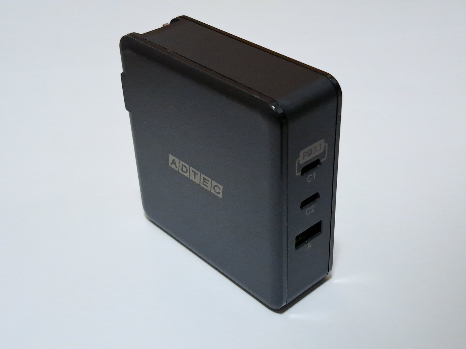 Black ADTEC charger with the upper USB-C socket labelled C1, lower USB-C socket C2, and rectangular USB-A socket A.